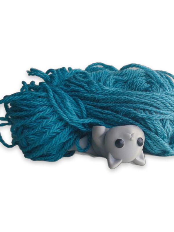 articulated-baby-cat-fidget-toy-poseable-desk-buddy-1 A white articulated cat figure lies curled in front of a skein of teal yarn.