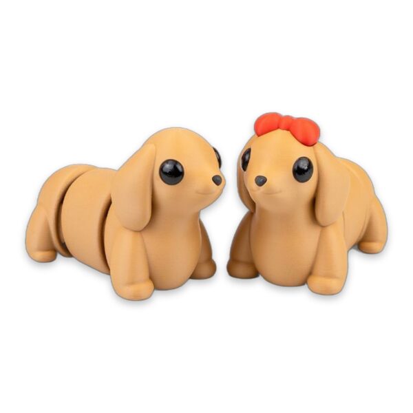 Two tan dachshund figures sitting side by side, one wearing a red bow on its head.