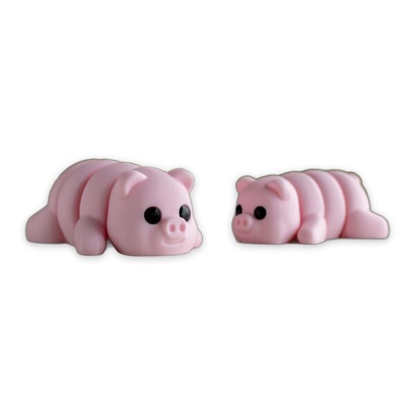 articulated-baby-pig-fidget-toy-poseable-desk-buddy-1 Two pink articulated baby pig figures lying on a table with greenery blurred in the background.