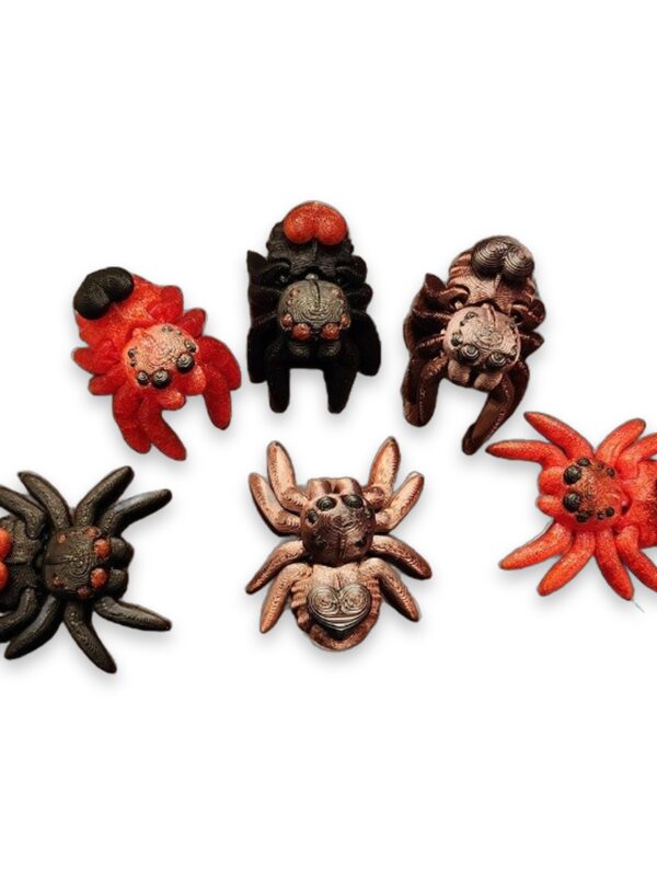 Six articulated heart spiders in red, black, and copper tones arranged on a marble surface.