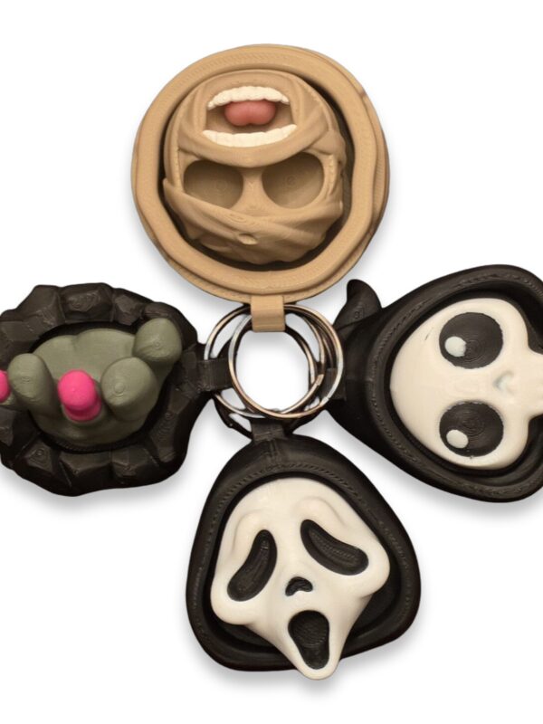halloween-clickers-fidget-toy-clickable-4 Four Halloween fidget clicker keychains arranged together: a mummy face, a clawed hand, a hooded skull, and a screaming ghost face.